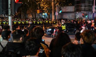 People gather as police officers block Wulumuqi street, named for Urumqi in Mandarin, in Shanghai on November 27, 2022