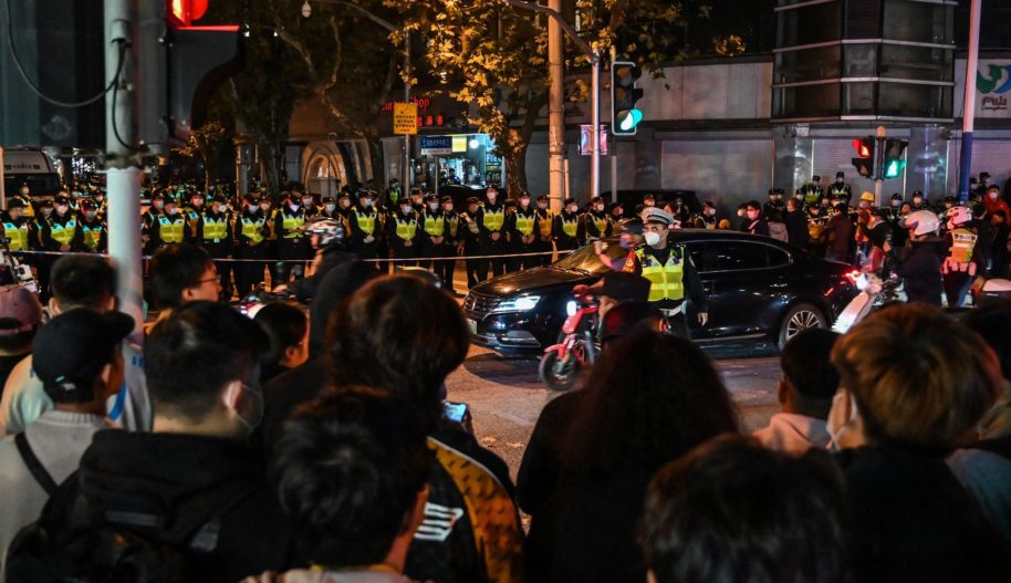 People gather as police officers block Wulumuqi street, named for Urumqi in Mandarin, in Shanghai on November 27, 2022